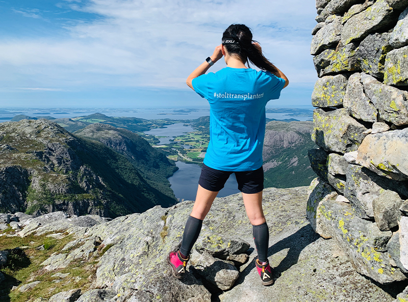 Bildet av Eileen på en fjelltopp som skuer ut over havet. På t-skjorten står det #stolttransplanter