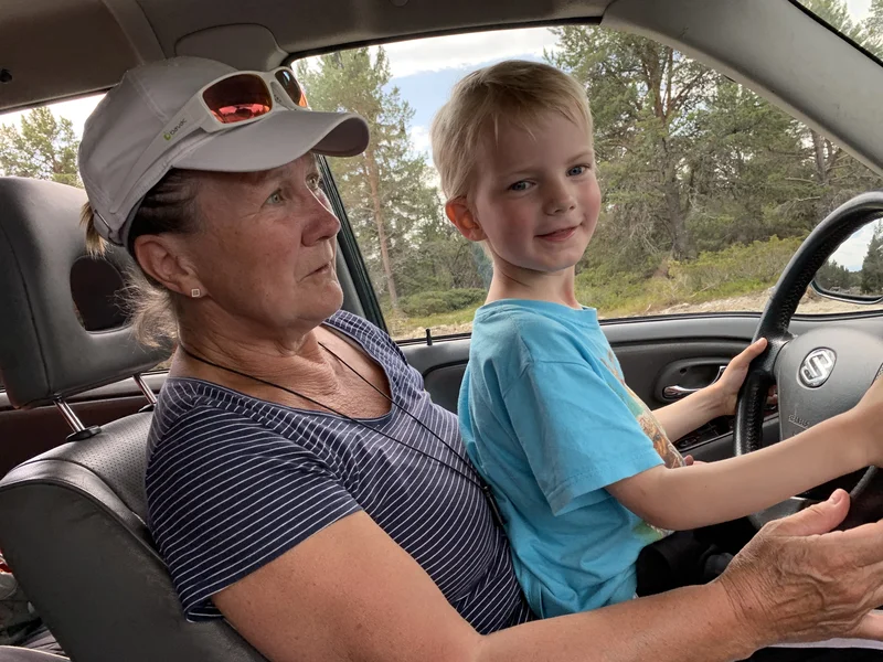 Alice Tungen sittende bak rattet i en bil med barnebarnet Edvin på fanget